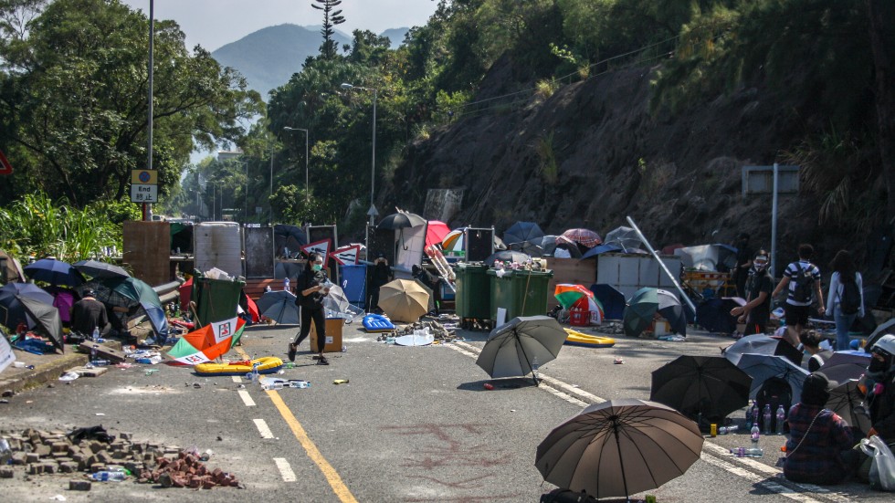 Demonstranterna har barrikaderat de tre infarter som finns till universitetet och belägrat hela universitetsområdet. Konflikten grundar sig i att man är orolig för att fastlandskina ska få för stort inflytande över Hongkong.