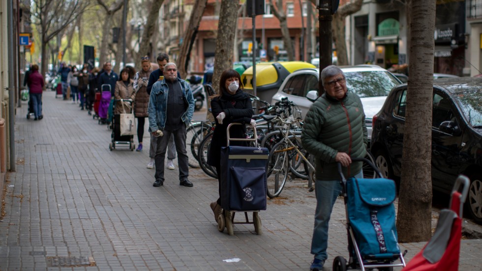 Människor i Barcelona, Spaniens näst största stad, köar på behörigt avstånd från varandra för att få handla mat på fredagen.