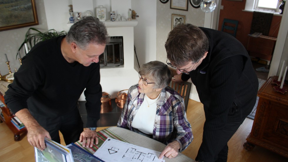 86-åriga Ebba Jonsson vill flytta från villan i Kvarnvik, men inte lämna bygden. Jörgen Nilsson och sonen Conni Jonsson visar skisser på sitt gemensamma projekt, Kvarnviks strand. 