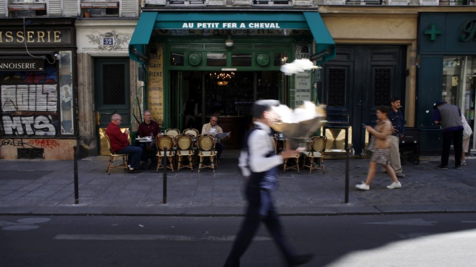 En man passerar med en bukett blommor framför ett café i stadsdelen Marais i Paris. Bild från september 2019.