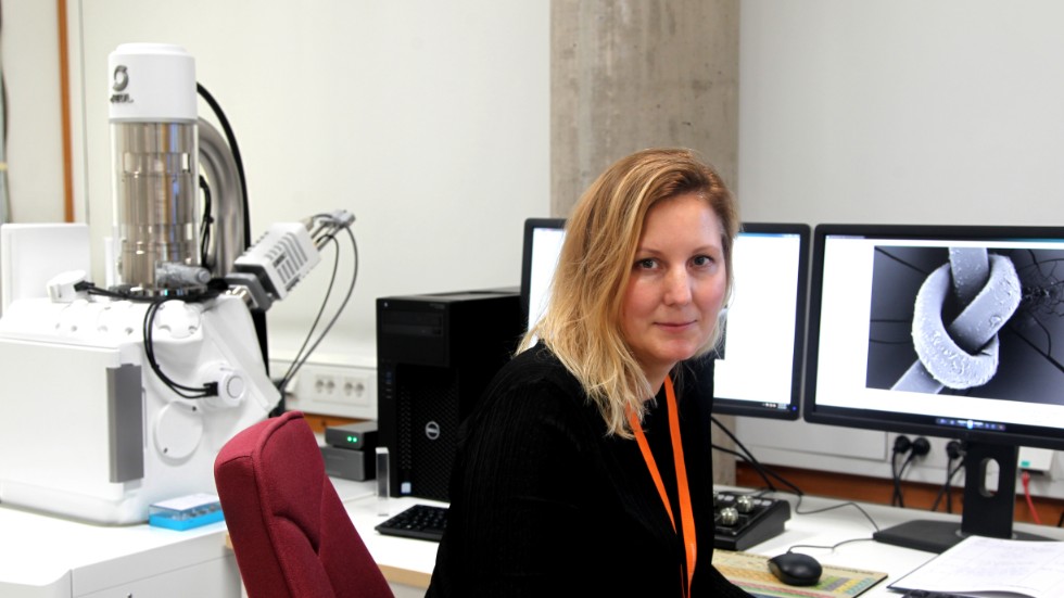 Sara Norrehed, kemist vid RAÄ, framför en förstorad bild av ett hårstrå med knut. T.v. ett svepelektronmikroskop. 