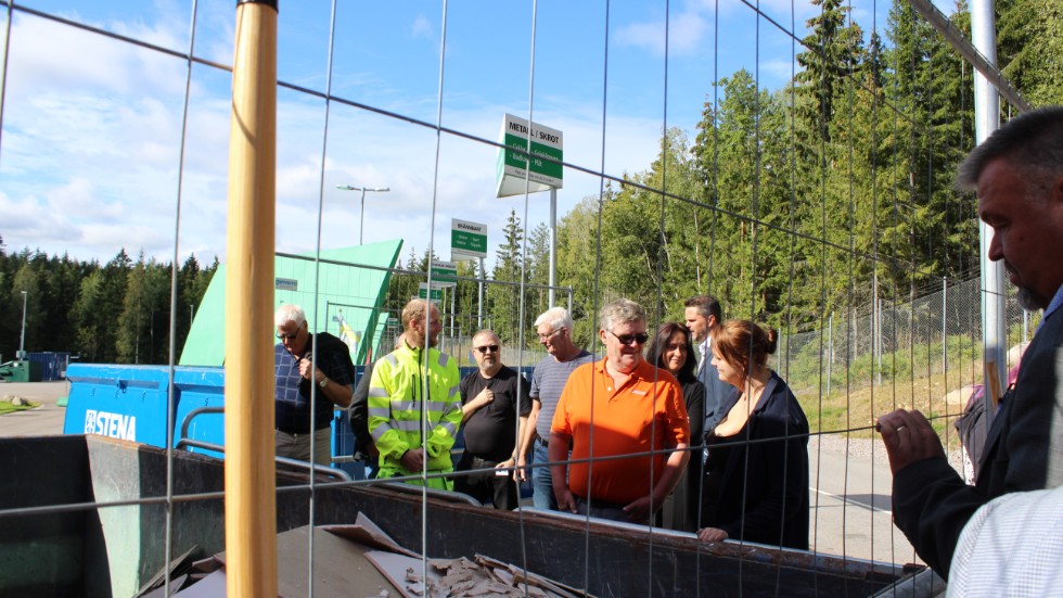 Delar av kommunstyrelsens ledamöter kikar ner i en container på återvinningscentralen i Korshult. Många ger beröm för att anläggningen är ren och välstädad. 