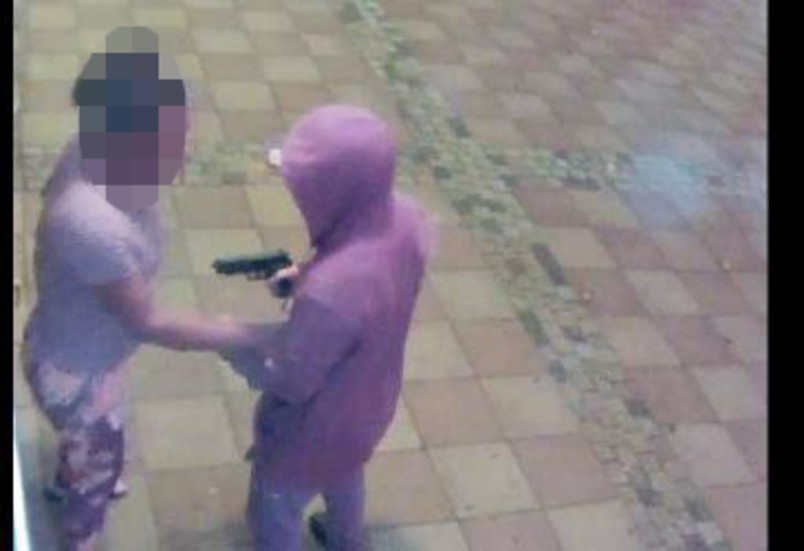 Här ses hur en rånare hotar en kvinna vid uttagsautomaten vid Skarphagens centrum.