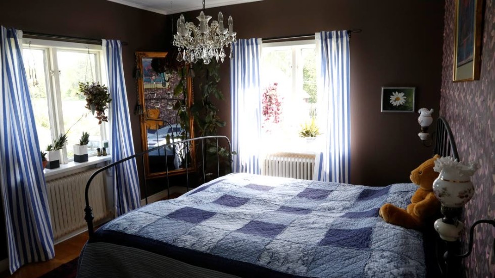 Sovrummet går i blått till bruna väggar, med vackert lapptäcke på sängen och blåvitrandiga gardiner.