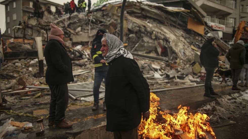 Människor försöker värma sig runt en eld vid av de många raserade byggnaderna i den turkiska staden Malatya.