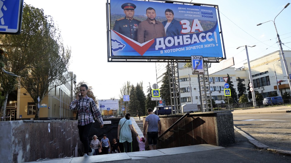 Människor vid en tunnelbanenedgång nära en rysk valaffisch i Donetsk.
