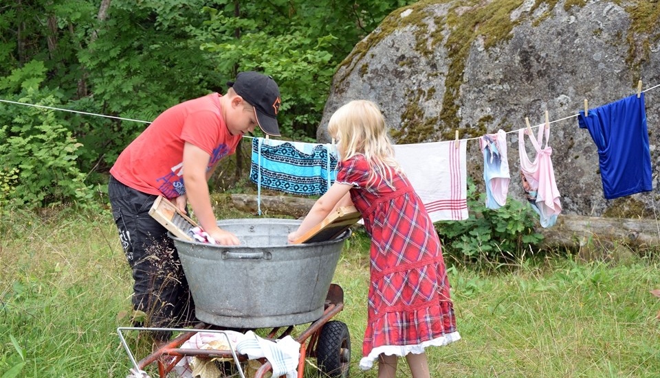 Syskonen Helmer och Vera Landberg testar att tvätta med hjälp av balja och tvättbräda.