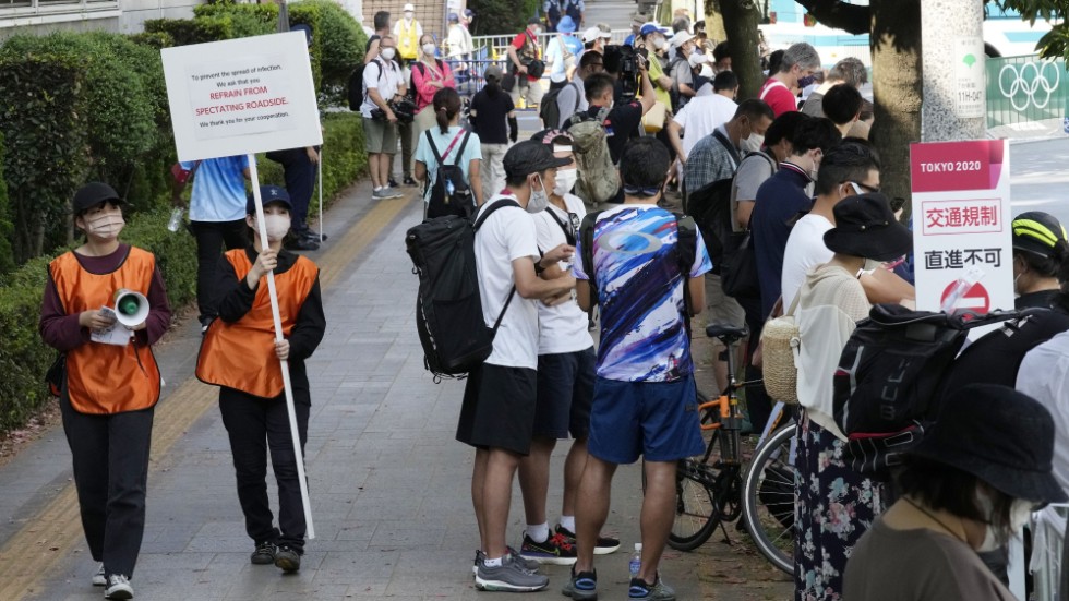 Funktionärer går omkring med skyltar som uppmanar folk att stanna hemma vid OS-triathlon i Tokyo.