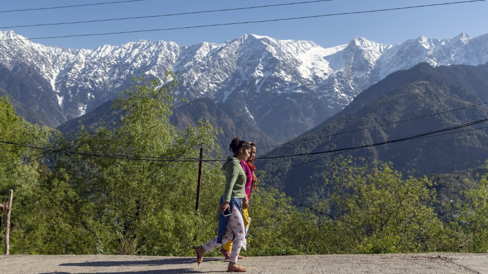 Promenerande kvinnor framför de snö- och istäckta Dhauladhar-bergen i Himalaya.