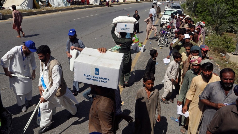 Flyende familjer som tagit skydd vid en väg i Charsadda, Pakistan, tar emot matpaket.