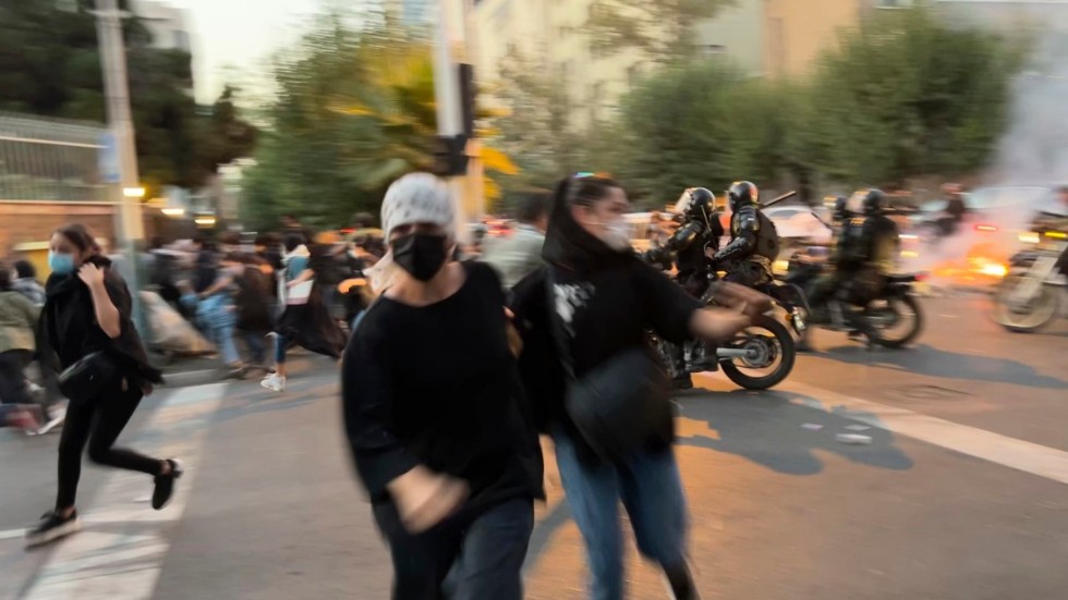 Två kvinnor och flera andra personer flyr när iransk kravallpolis kör emot dem på motorcyklar, vid en av de tidiga protesterna i Iran i september förra året. Arkivbild.