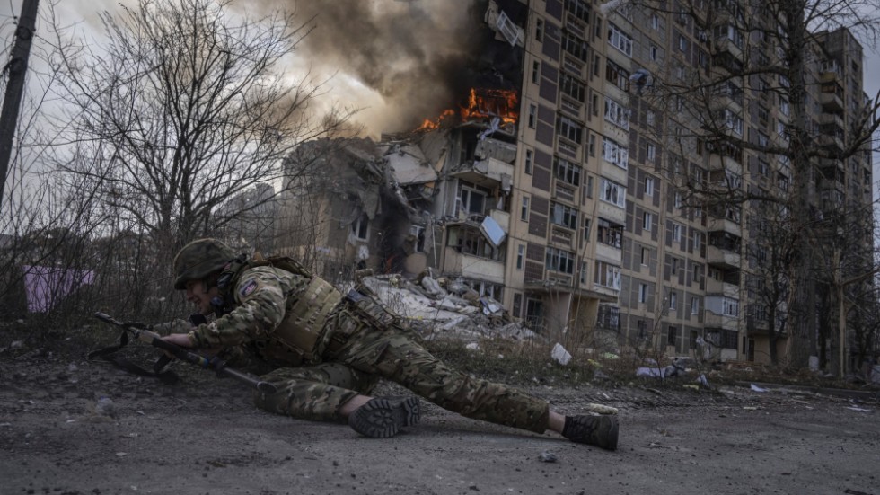 En ukrainsk polis tar skydd framför en brinnande byggnad i Avdijivka i fredags.