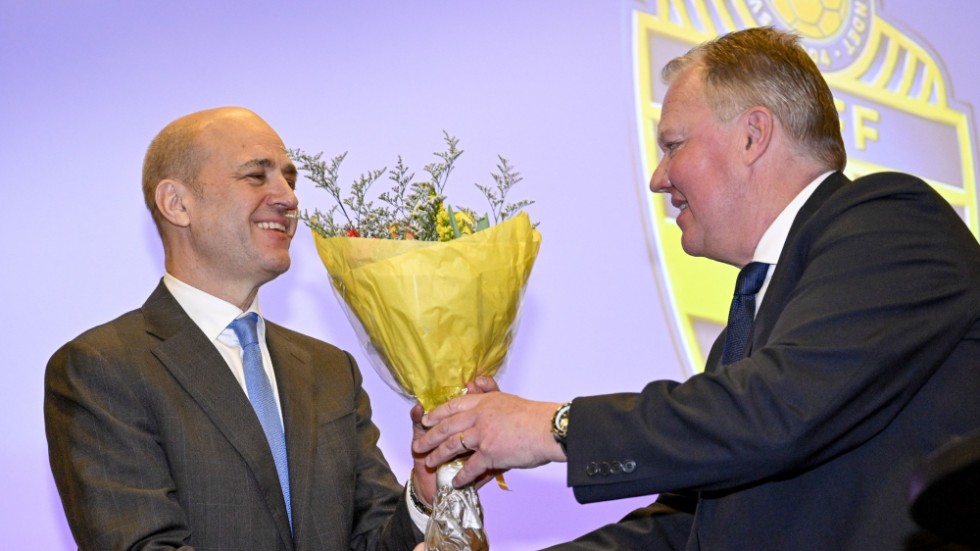 Avgående ordföranden Karl-Erik Nilsson räcker över en blombukett för att gratulera.