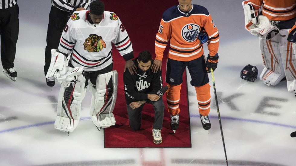 Minnesotas Matt Dumba står på ett knä under USA:s nationalsång, flankerad av Chicagos Malcolm Subban och Edmontons Darnell Nurse, när NHL inledde playoffserien med att markera mot rasism.