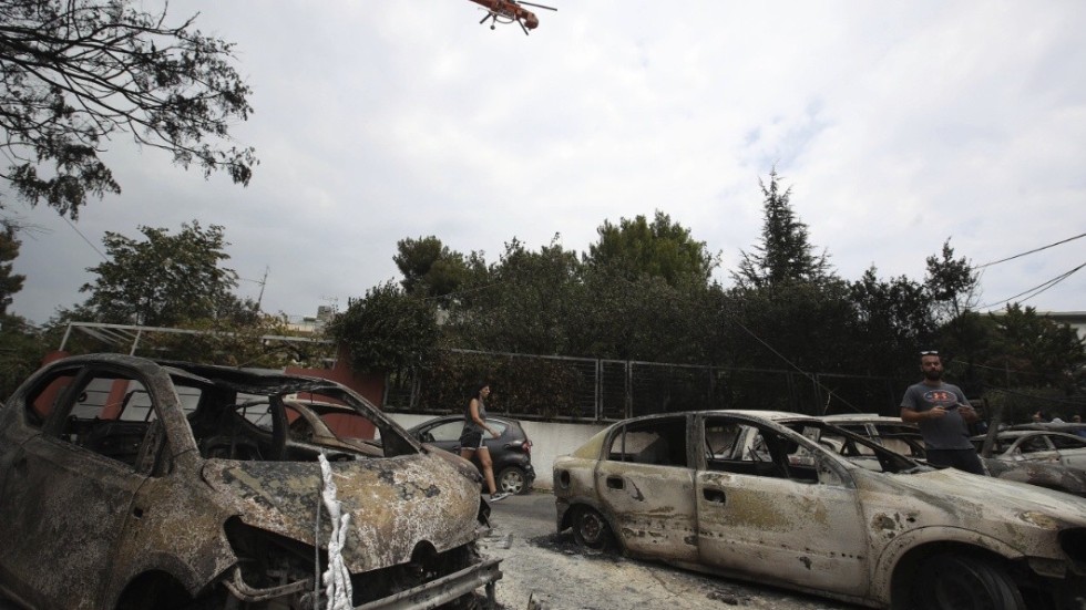 A firefighting helicopter flies above burned-out cars in Mati east of Athens, Tuesday, July 24, 2018.
