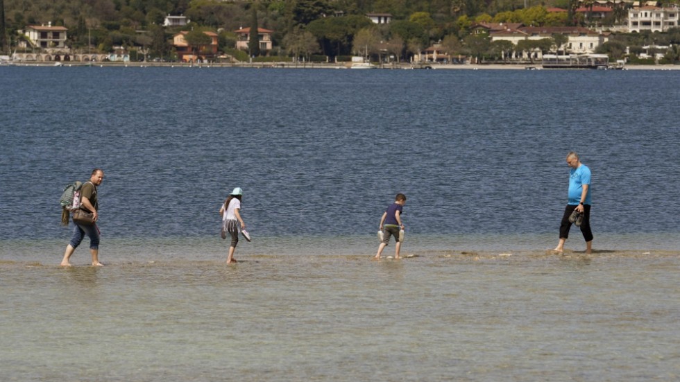 En grupp turister promenerar från fastlandet till ön San Biagio i Gardasjön. Vattennivåerna i den italienska insjön är extremt låga.