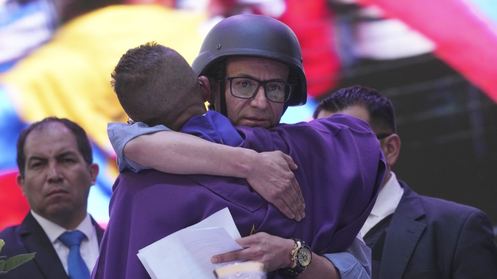 Presidentkandidaten Christian Zurita, iklädd skyddsväst och hjälm, kramar om en katolsk präst under ett valmöte i Quito i torsdags. Zurita har klivit in som ersättare för den mördade kandidaten Fernando Villavicencio.