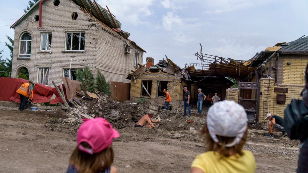 Två barn tittar på medan hjälparbetare städar upp efter ett bombnedslag i Kramatorsk i Donetsk. Bilden är tagen 12 augusti.