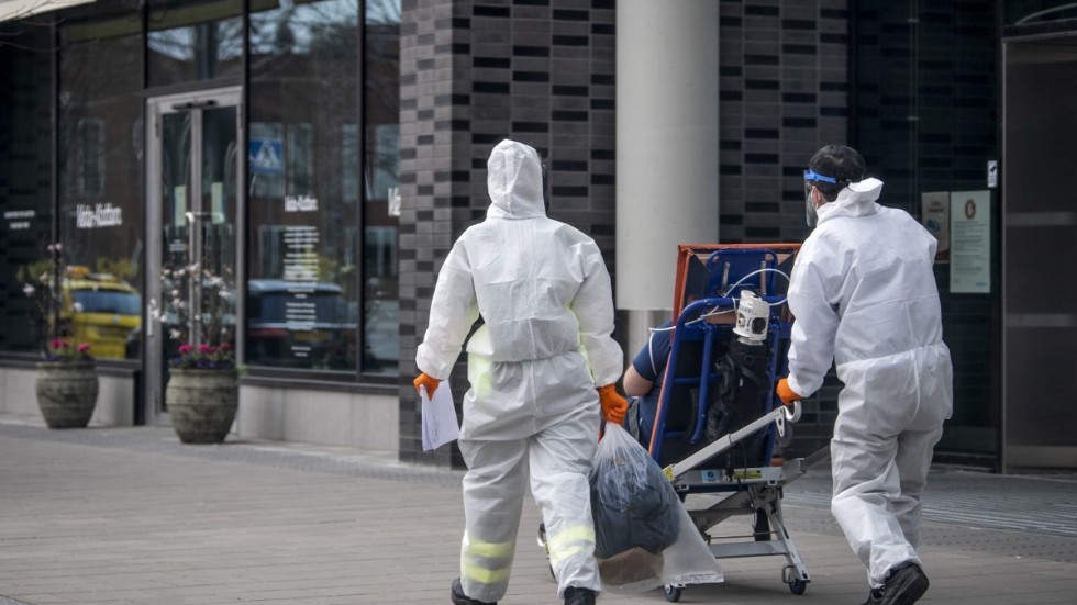 Personal iklädda skyddskläder hjälper en patient in på Karolinska sjukhuset i Solna i april. Arkivbild.