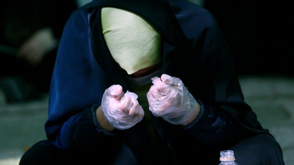 En kvinna iförd ansiktsmask och handskar är försjunken i bön i en moské i Irans huvudstad Teheran.
