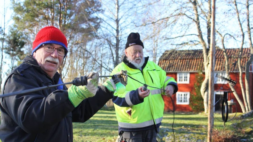 Lasse Vigertsson och Roland Thorstensson hänger upp de kulörta lamporna, som bidrar till att det blir juligt och mysigt i parken på lördag.
