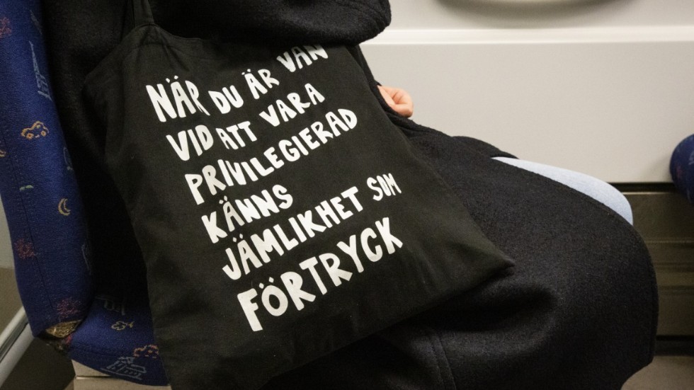 Privilegiet att leva i ett gott samhälle är inte ett gott liv, utan att med klar blick, fri från hunger och nöd, kunna se det goda livets historia exakt för vad det är: ett liv på andras bekostnad, skriver Christopher Paulstam.
Bilden: Kvinna på tunnelbanan med tygkasse med texten "När du är van vid att vara privilegierad känns jämlikhet som förtryck", av konstnären Jessica Hallbäck.  

