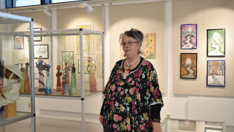 Minka Eriksson ställer ut på biblioteket i Kisa. I bakgrunden syns några av hennes tavlor. I montern syms figurer som hon tillverkat i kallporslin.