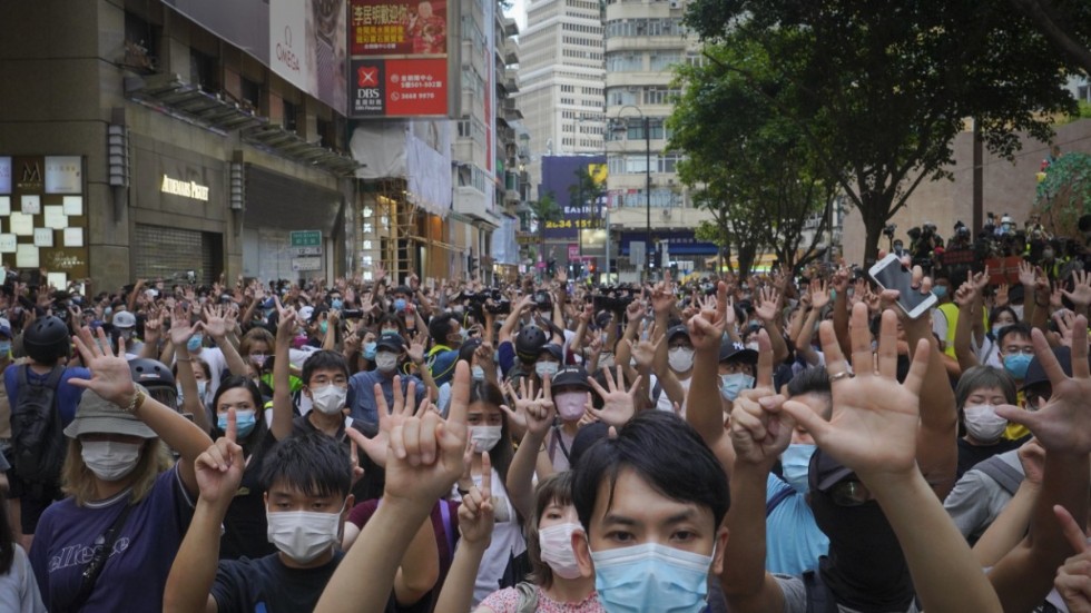 Demonstranter ute på Hongkongs gator i går i protest mot säkerhetslagen. Handgesterna betyder "Fem krav och inte ett färre". Det syftar på de krav demonstranterna ställde vid protesterna i höstas.