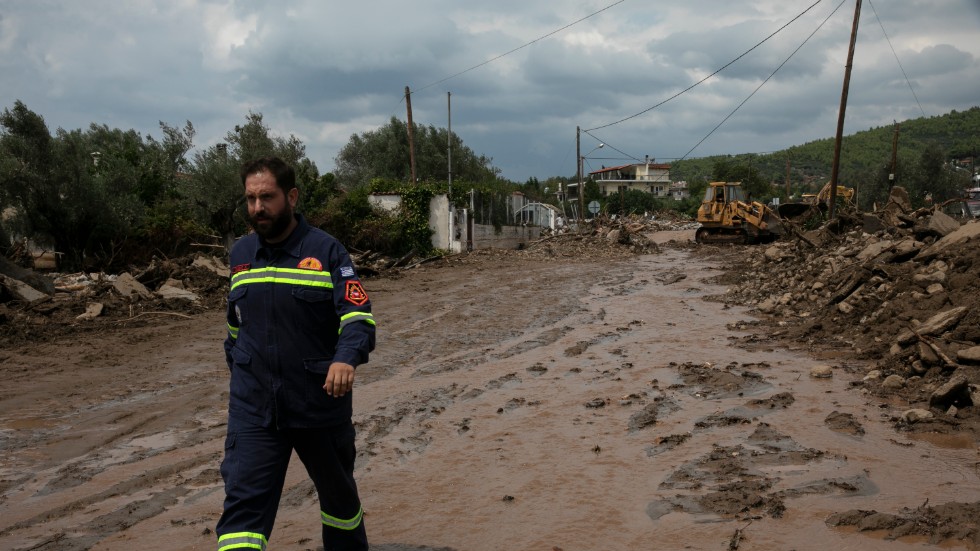 En räddningsarbetare går på en förstörd väg i byn Politiká som drabbats hårt av regnet.