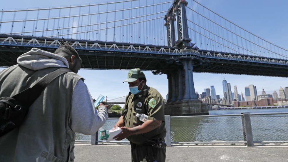 En parkvakt delar ut munskydd vid parkområdet under Brooklyn Bridge i New York.