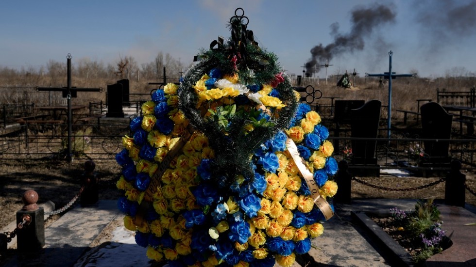 Motstånd. Blommor på en kyrkogård utanför Kiev, med rök från en artilleriattack i bakgrunden.