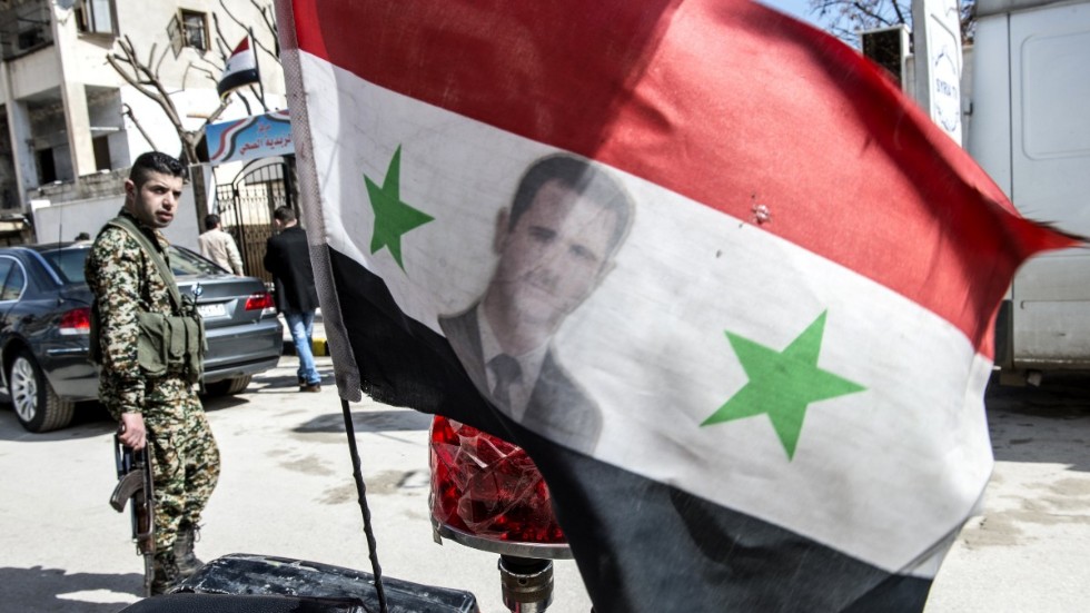 Östra Aleppo. Flagga med president Bashar al-Assad och regeringssoldat i bakgrunden. Bild från 2017.
