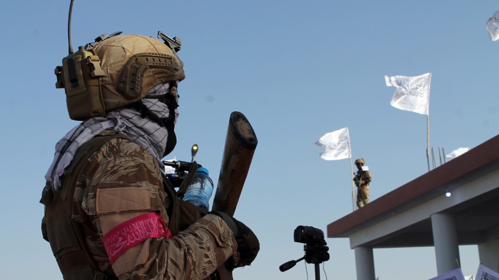 En talibankrigare står vakt i Lashkar Gah, södra Afghanistan, medan rörelsens vita fanor vajar i bakgrunden.