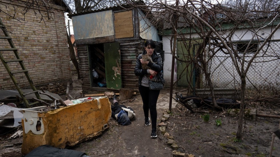En kvinna går över en innergård och håller i sin katt. På marken ligger hennes man och hennes bror som dödats i Butja, utanför Kiev.