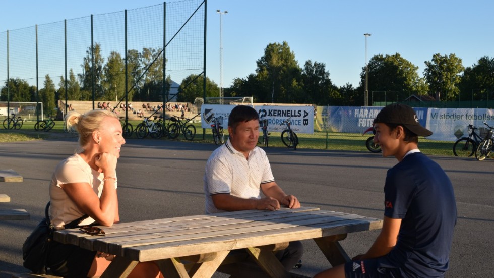 Jenny Rönningen, Ismail och Murteza Panahi sitter i kvällsolen utanför Hackelhallen i Rimforsa. 