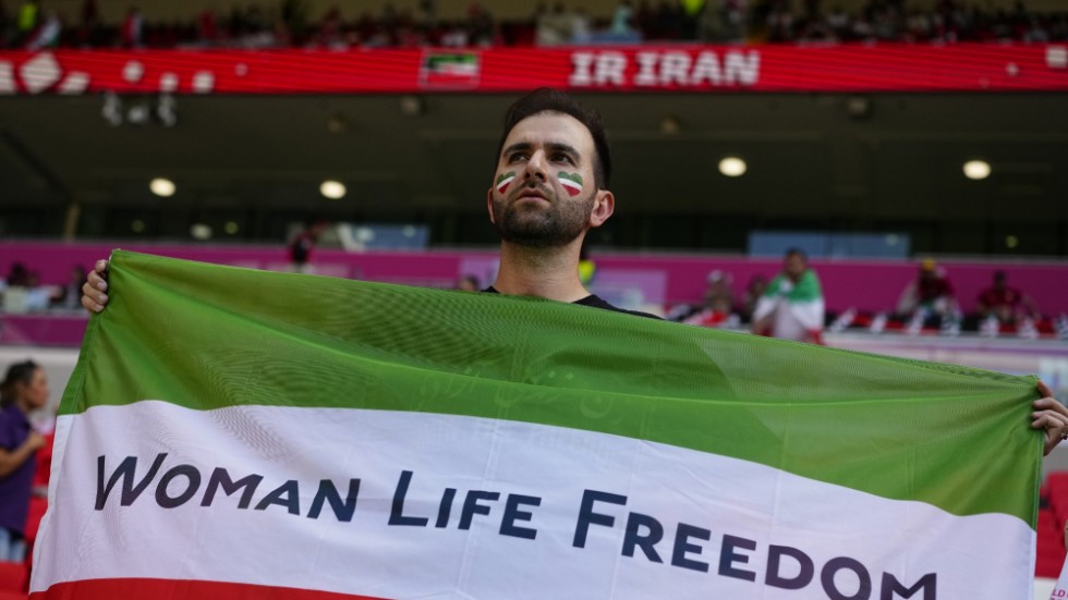 En iransk supporter håller upp en flagga med den iranska proteströrelsens slagord på läktaren.