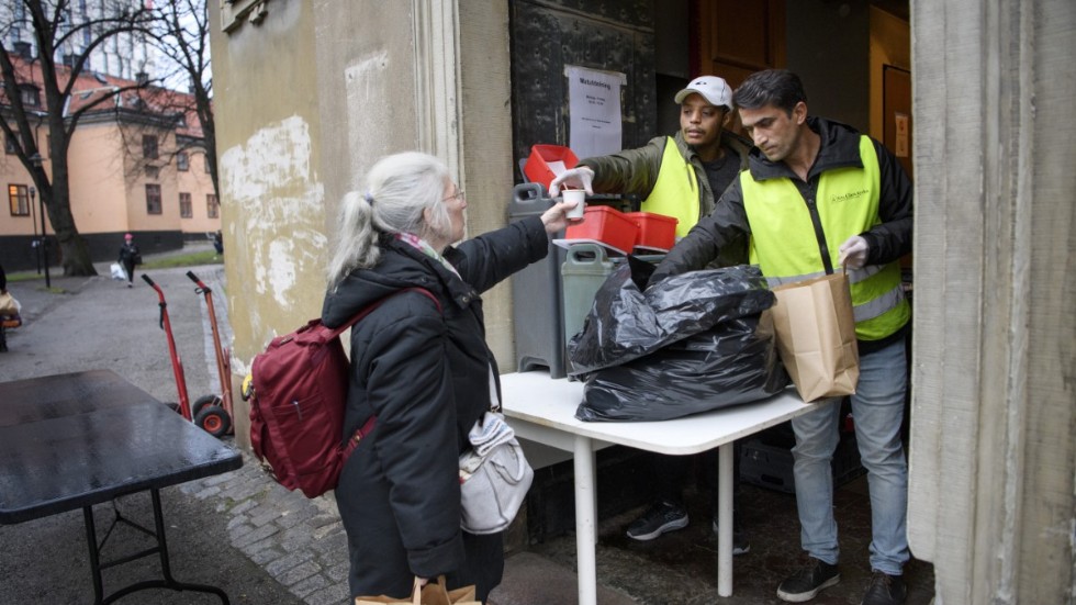 Mia Johansson får en kopp kaffe och en påse med mat av Bajo Gabrimariam och Wahid Nafipour vid St:a Clara kyrka, som delar ut mat till hemlösa.
