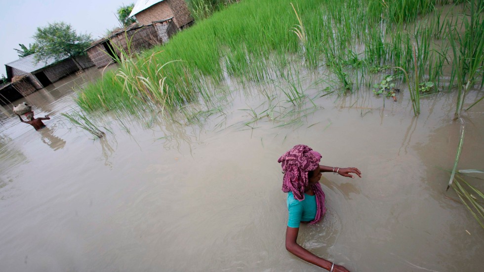 Lokalbefolkning vadar i vatten efter en tidigare översvämning i Bangladesh. Arkivbild.
