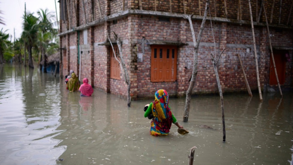 Invånare i byn Pratap Nagar i Bangladesh vadar genom vattenmassor för att ta sig till sina hem. Översvämningar blir vanligare i klimatförändringarnas spår. Arkivbild.