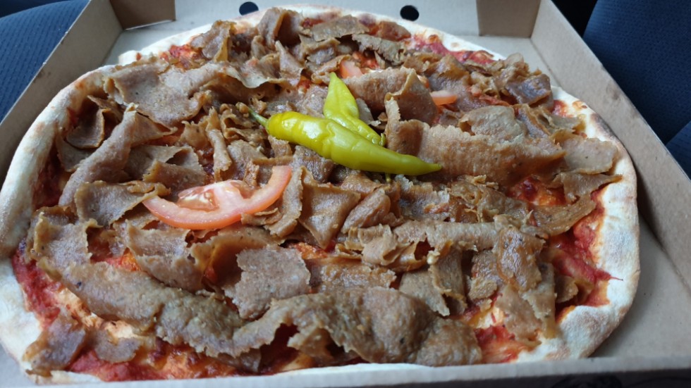 A kebab pizza, with a stray slice of tomato.