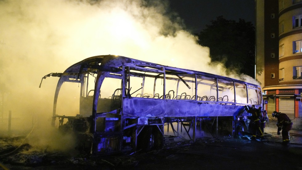 Brandmän släcker glöden i en buss som förstörts i en brand i Nanterre utanför Paris, under natten till lördag.