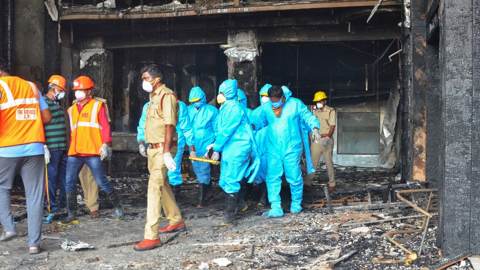 Räddningsarbetare i skyddskläder bär ut en kropp från det elddrabbade hotellet Swarna Palac.
