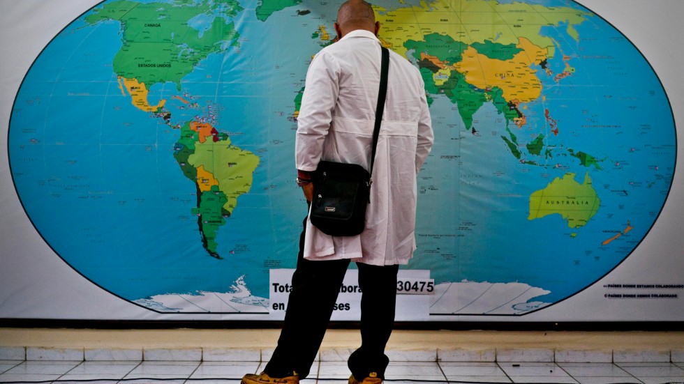 En läkare från Kubas Henry Reeve Internationella Medicinska Brigader blickar ut över en världskarta innan avresa till ett av brigadens viktiga uppdrag. 