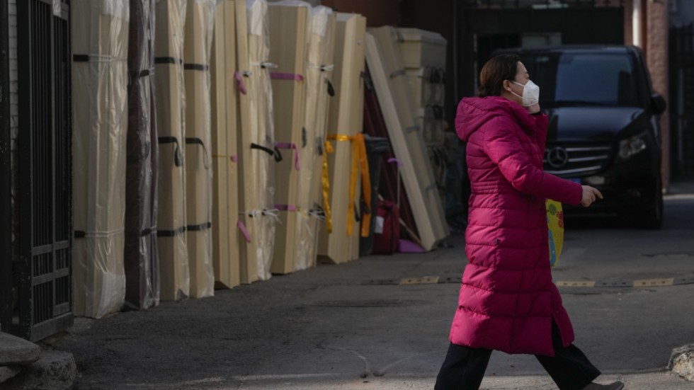 En kvinna med andningsskydd går förbi tomma kistor vid ett bårhus i Peking.