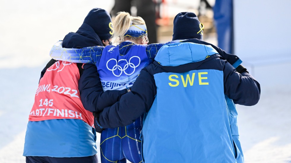 Frida Karlsson får hjälp av svenska ledare att ta sig ut från målområdet efter milloppet i OS.