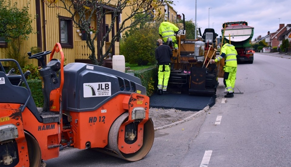 Till vänster övervakar Kevin Lindström arbetet mot staketet medan Lukas Brangenfeldt kör asfaltsläggaren och Alexander Holm justerar högersidan ut mot gatan.