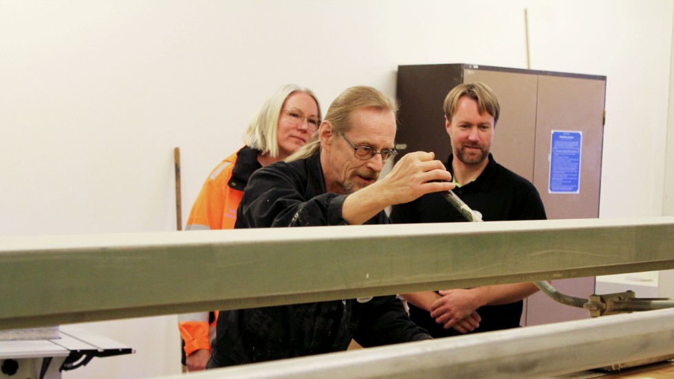 Handledaren Markku Heikkinen placerar ett bord i slipen. Miljöingenjör Martina Hornwall och arbetsledaren Mattias Borup tittar på.