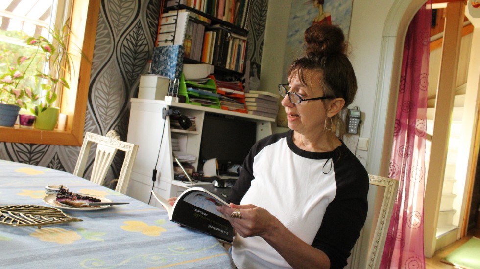 Stina Nilsson Bassell bläddrar i "Kärleken är en sekatör". Bakom henne målningen som pryder omslaget.